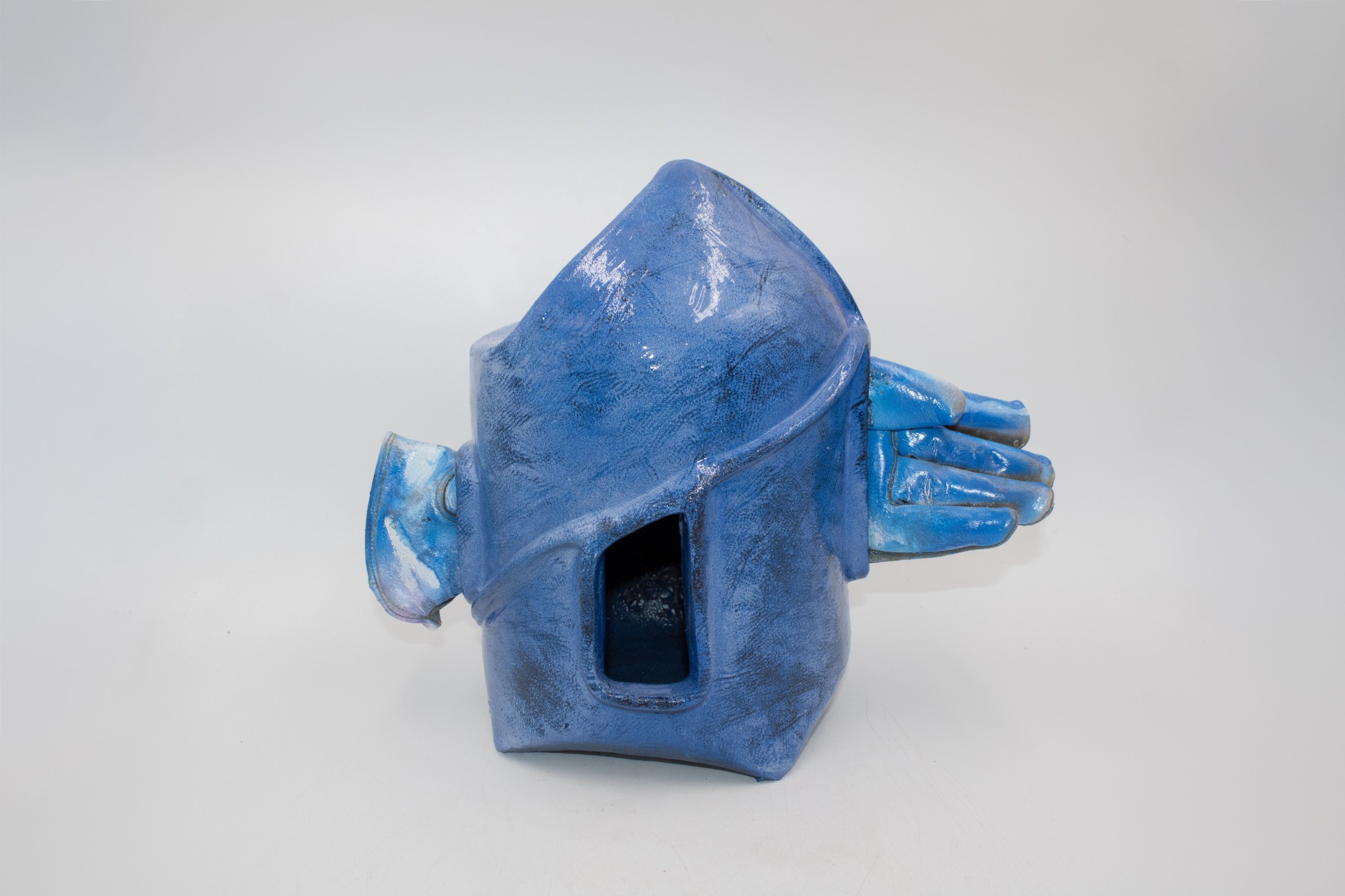 A hand-built ceramic vessel with a tilted roof-like form and an open doorway at the center. The opening reveals a dark interior, suggesting both absence and an invitation to enter, reflecting an unstable sense of home.