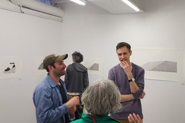 Three people in a gallery talking and one person looking at the art on the white walls.