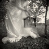 A black and white photo of a a large fabric cloth in movement, in the woods.