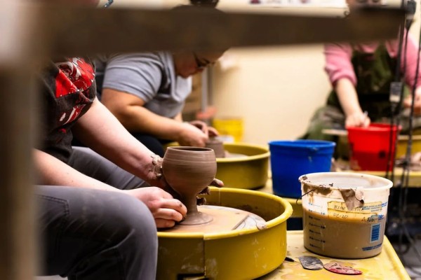 People creating pottery on a wheel in a studio.
