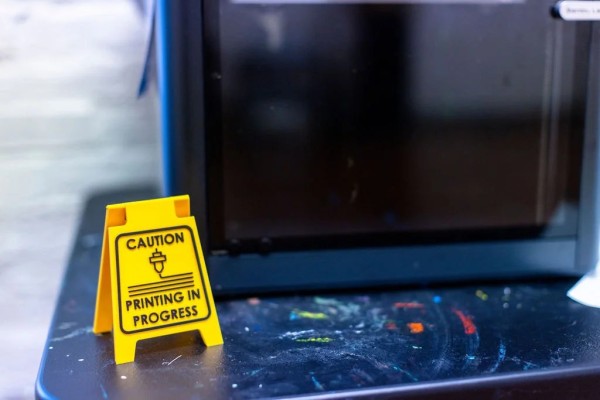 A table with a miniature yellow floor-caution sign stating 'Caution: Printing in Progress.'