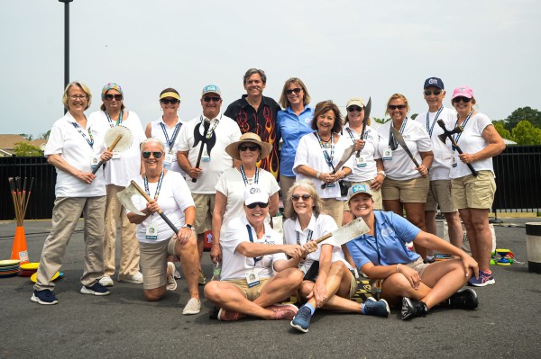 A group of people outside in white shirts holding prop medieval weapons and smiling at the camera.