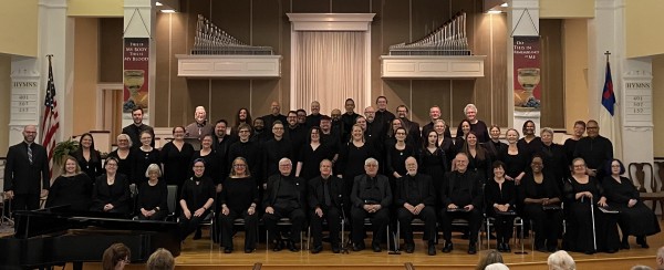A large group of people wearing all black in rows, at the front of a church inside.