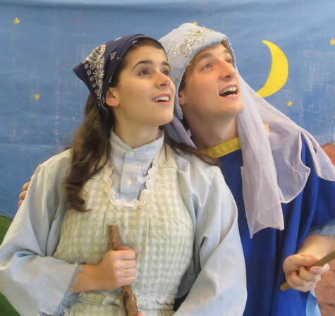 A woman and a man in old timey clothes and headscarves in front of a drawn nighttime backdrop, looking away from the camera.
