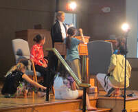 An adult teaching children film on stage.