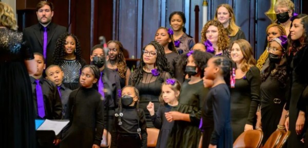 A group of young people in a choir, wearing all black on a stage, performing.