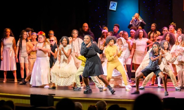 A big group of children in costumes performing and dancing on stage.