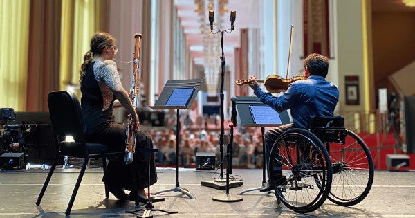 Two musicians on stage playing instruments, with one on the right playing the violin in a wheelchair.