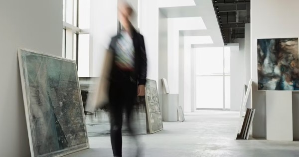 A person in motion walking through an art gallery with paintings leaning on the walls.