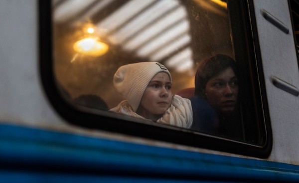 A photograph of a child and mother looking out of a train window, taken from outside.