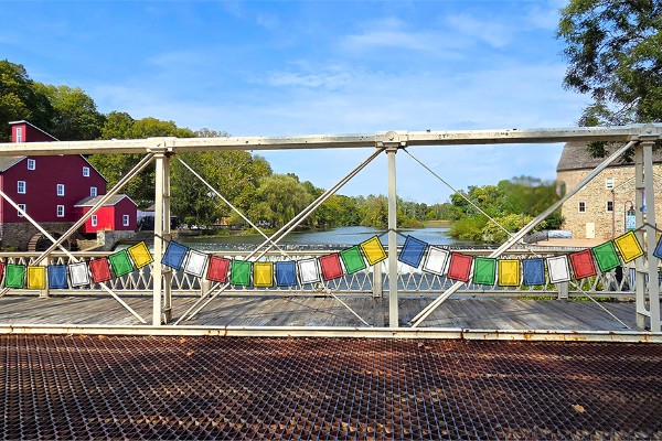 flags strung across the deck of a bridge with mills on each bank of the river